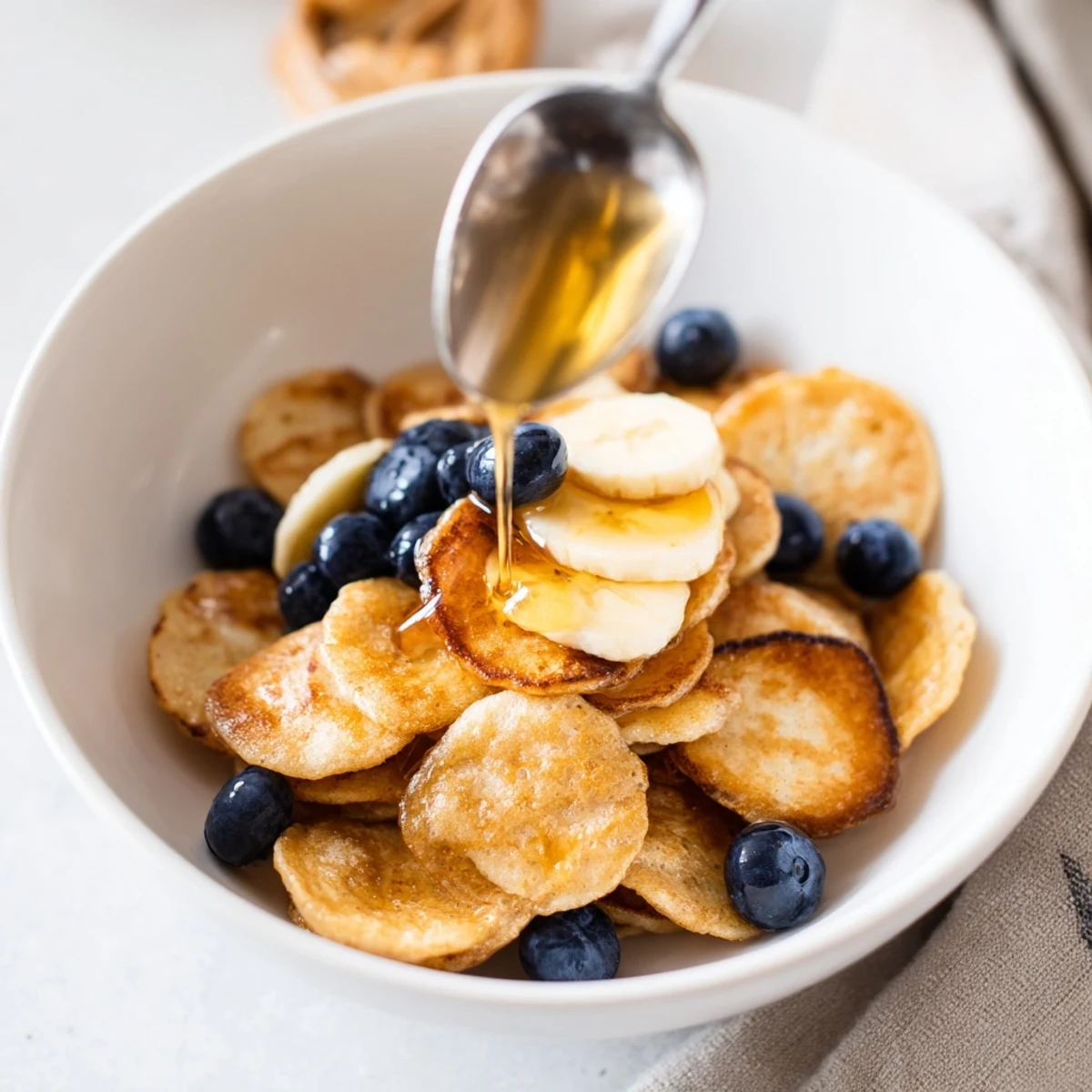 Adorable mini pancake cereal sprinkled with fruit and syrup for a tasty morning treat.