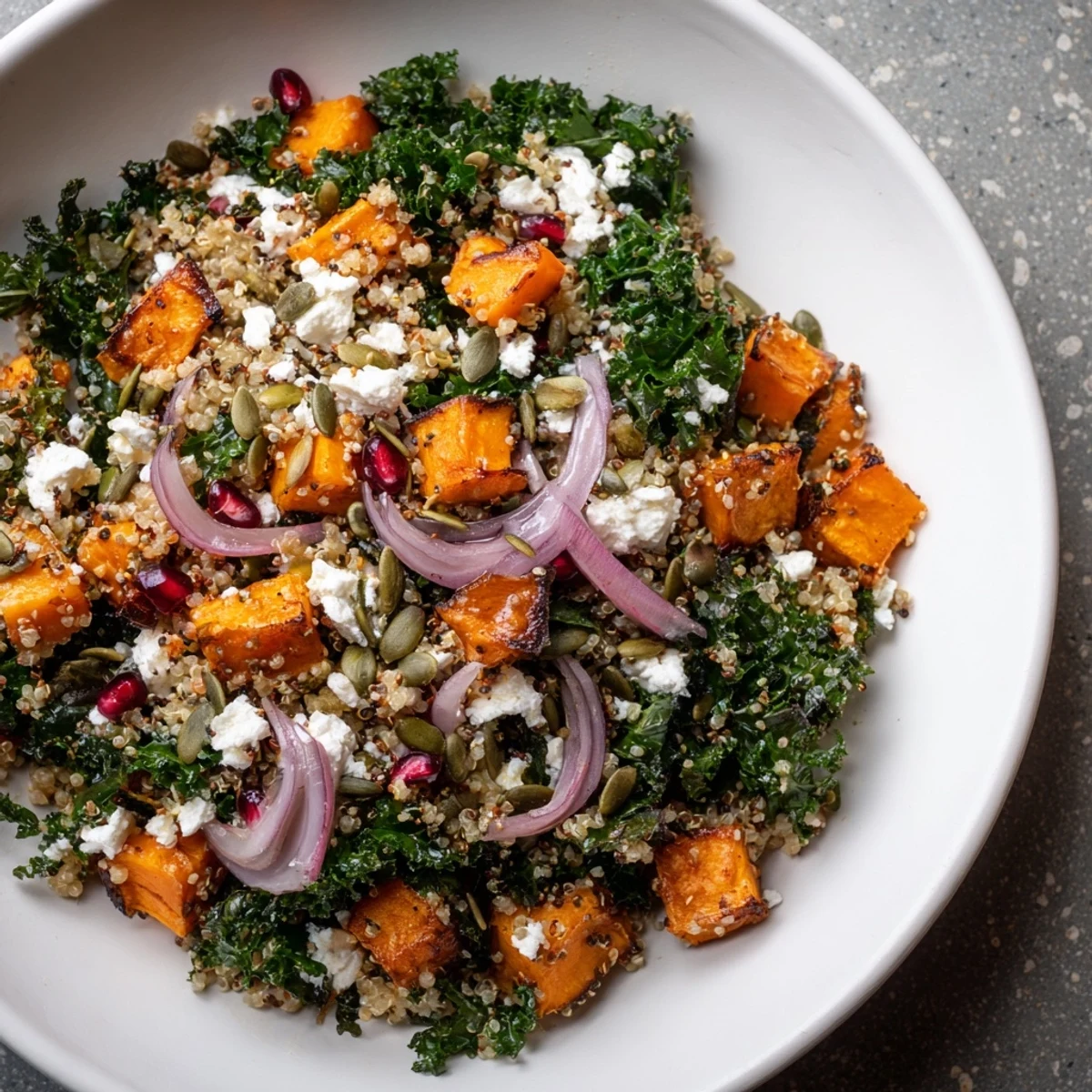 Delicious Kale & Quinoa Salad topped with pomegranate seeds, and crumbled feta, perfect for a healthy meal.