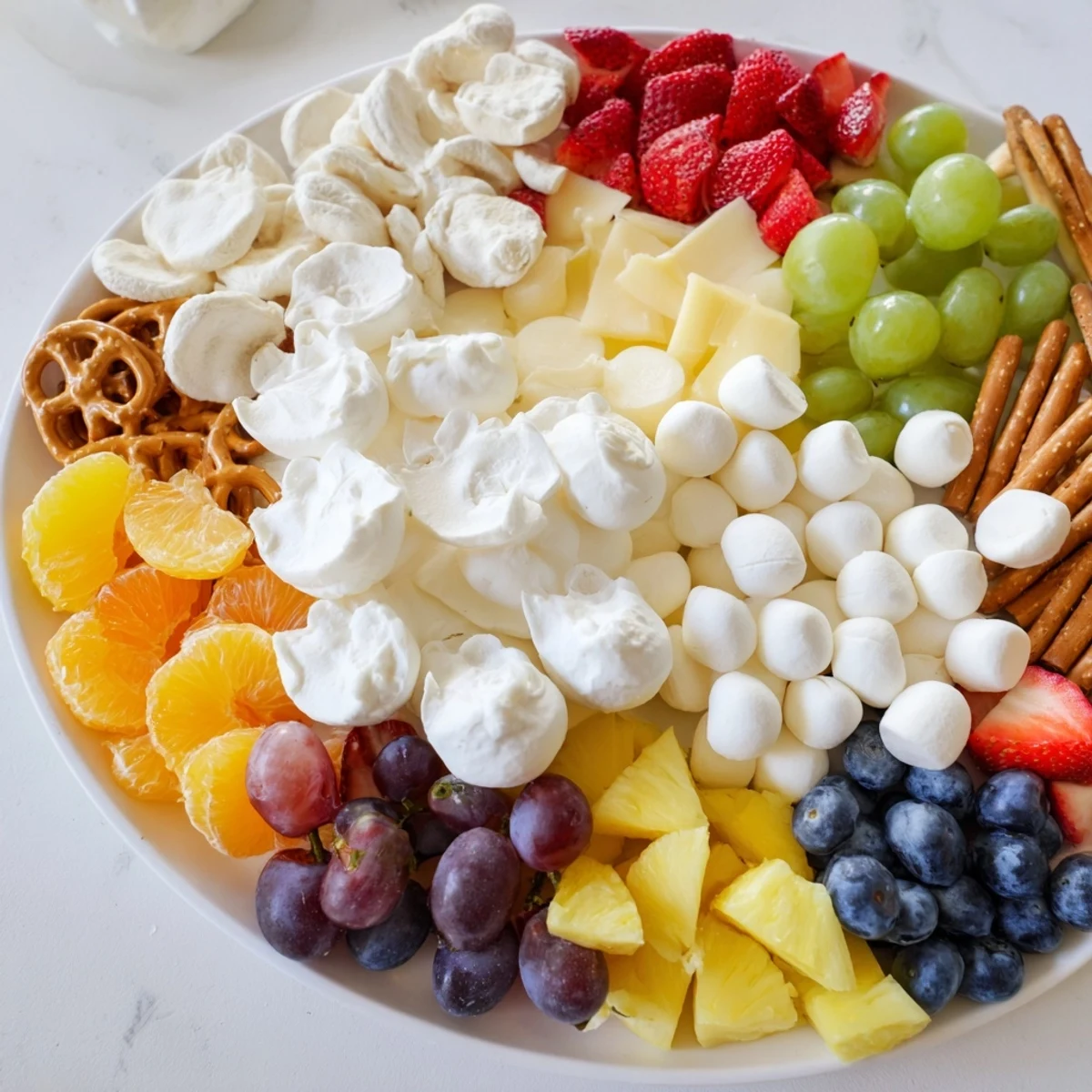 A vibrant Cloud & Rainbow Grazing Board: creamy cheeses and a colorful fruit rainbow for a party.