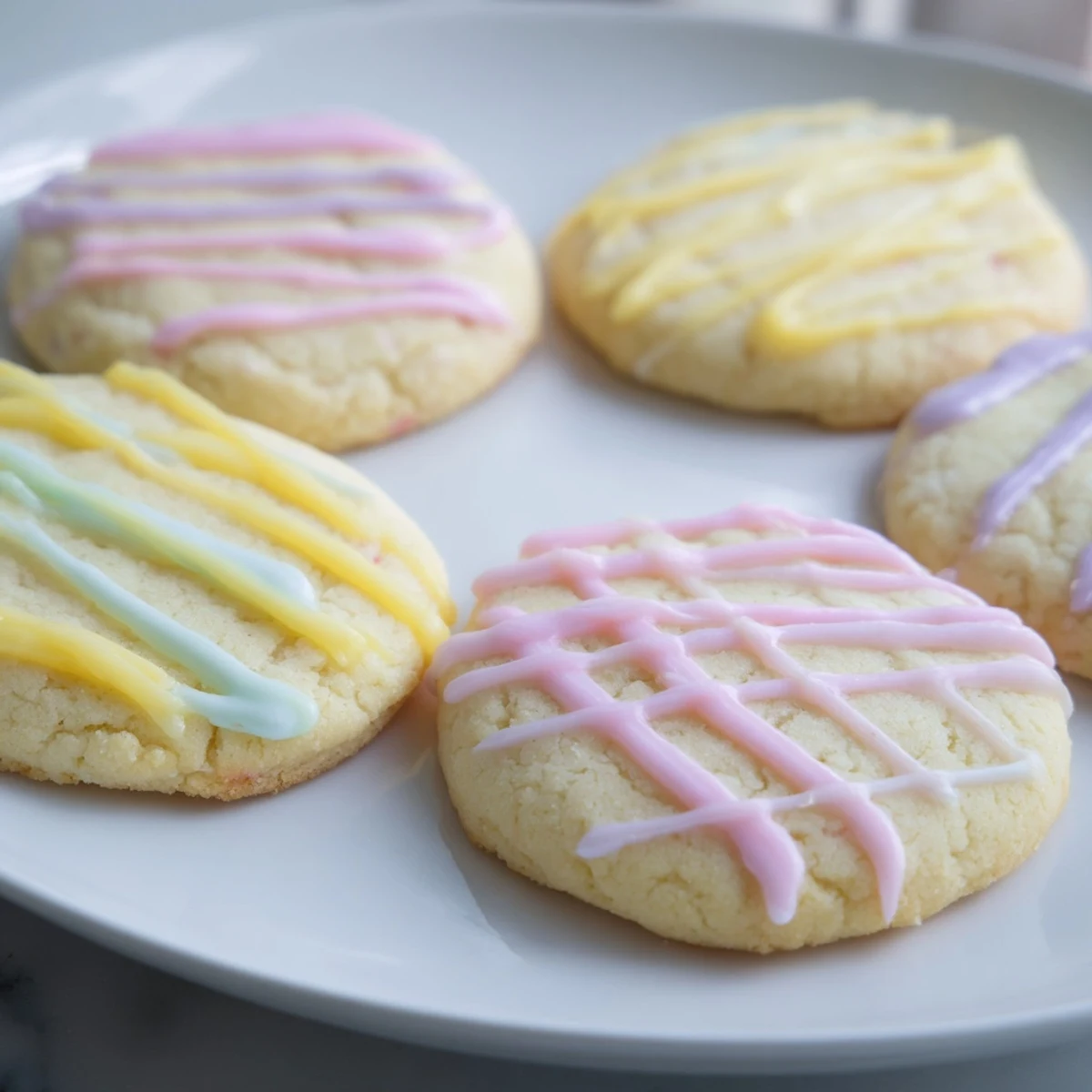 A plate of freshly baked sugar cookies with a colorful, swirled icing drizzle looks delicious.