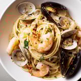 A close-up of steaming seafood linguine, pasta glistening with olive oil and fresh herbs.