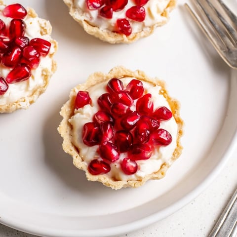 Mini pomegranate cream cheese tartlets topped with vibrant seeds and creamy filling.  