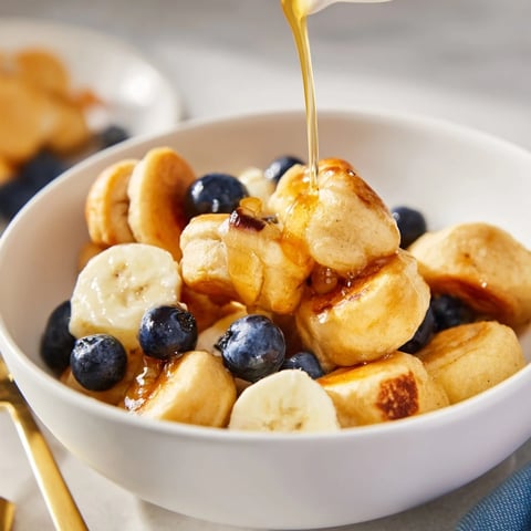 Mini pancake cereal drizzled with syrup and topped with fresh berries in a bowl.  