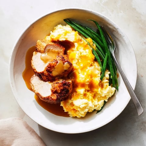 Juicy pork chops resting on creamy cheddar mash, drizzled with savory gravy.  