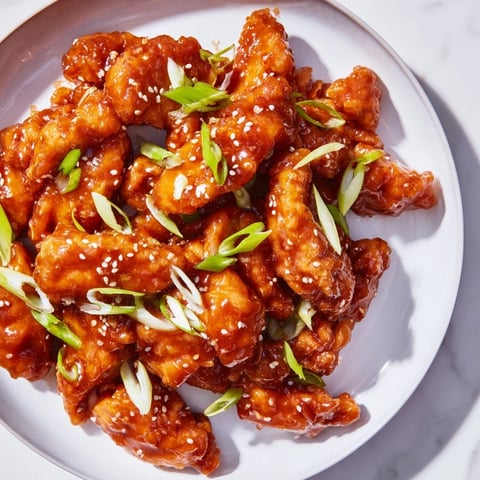 Skillet-seared sweet and spicy Sriracha Honey Chicken, glistening with a vibrant and flavorful glaze.