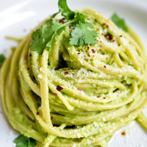 Bright green Smashed Avocado Pasta coated spaghetti, garnished with fresh basil, for a delicious lunch.