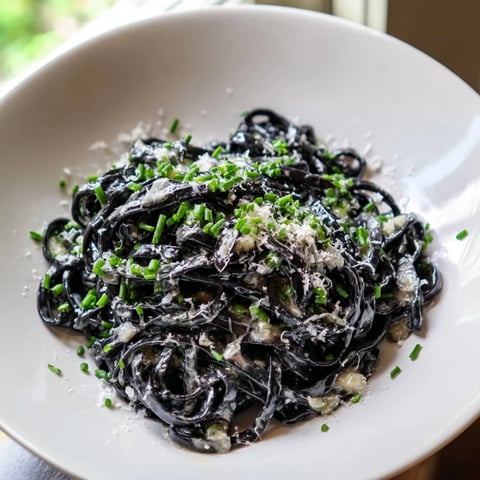 Dramatic squid ink pasta, a luxurious black pasta dish with creamy, glistening sauce and fresh herbs.