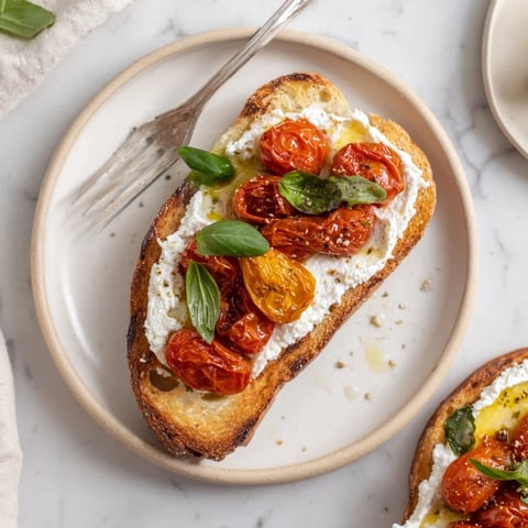 Creamy whipped ricotta and sweet roasted cherry tomatoes piled high on golden, crusty sourdough toast, garnished with fresh basil and a drizzle of olive oil.