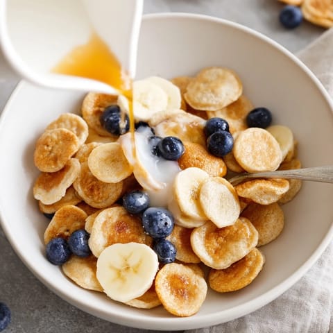 Bite-sized mini pancakes, golden and fluffy, served with milk for breakfast delight.  