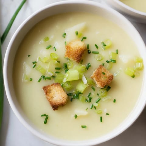 Close-up of golden Potato Leek Soup: Smooth, pureed texture with a swirl of cream.
