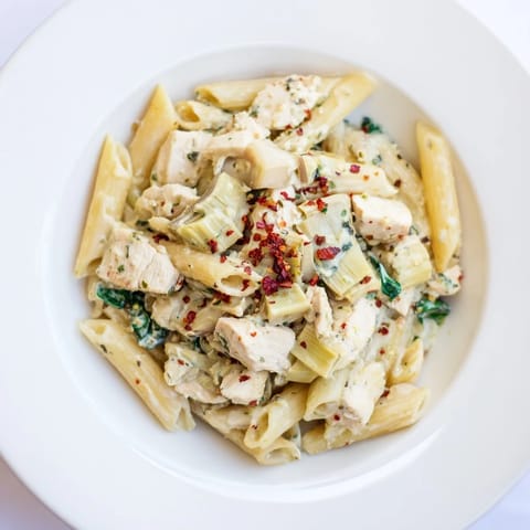 A close-up of Creamy Spinach Artichoke Protein Pasta Skillet: pasta twirled with spinach and artichokes.