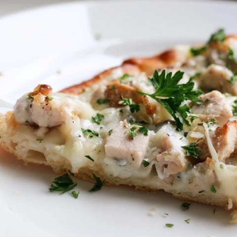 A close-up of Chicken Alfredo Pizza topped with fresh parsley, showing a cheesy slice ready to serve.