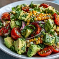 Fresh summer salad with sweet corn, juicy tomatoes, creamy avocado, and zesty lime vinaigrette, perfect for a light meal or side dish.  