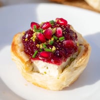 Warm golden Fireworks Brie Tartlets, oozing melted cheese, topped with festive pomegranate seeds and herbs.